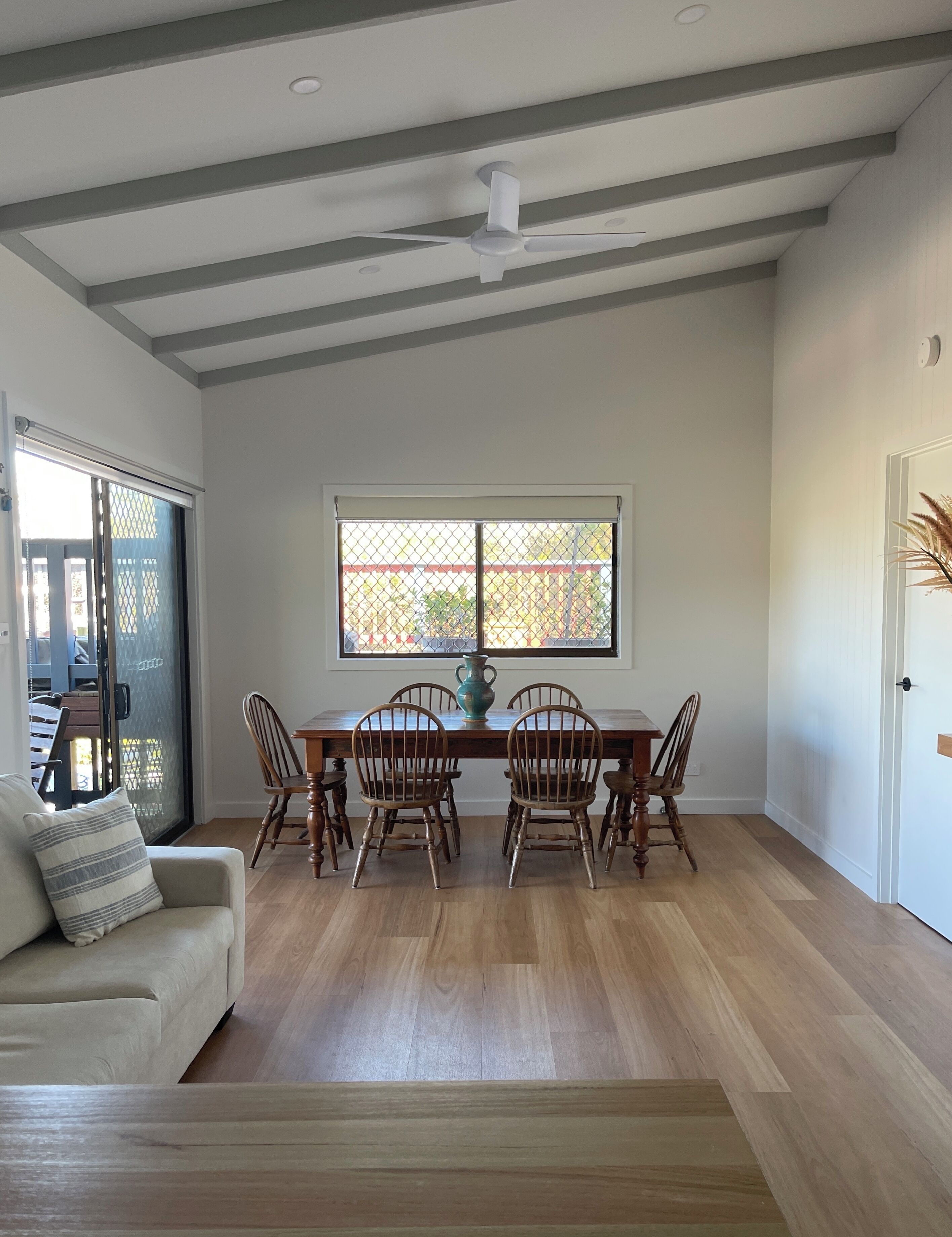 A dining area with a wooden table, four chairs, a vase, and a window with a view.