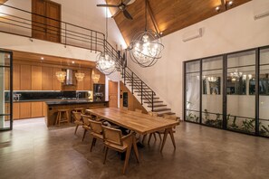 A spacious kitchen with a long wooden table and chairs, a staircase, and a large window with a view.