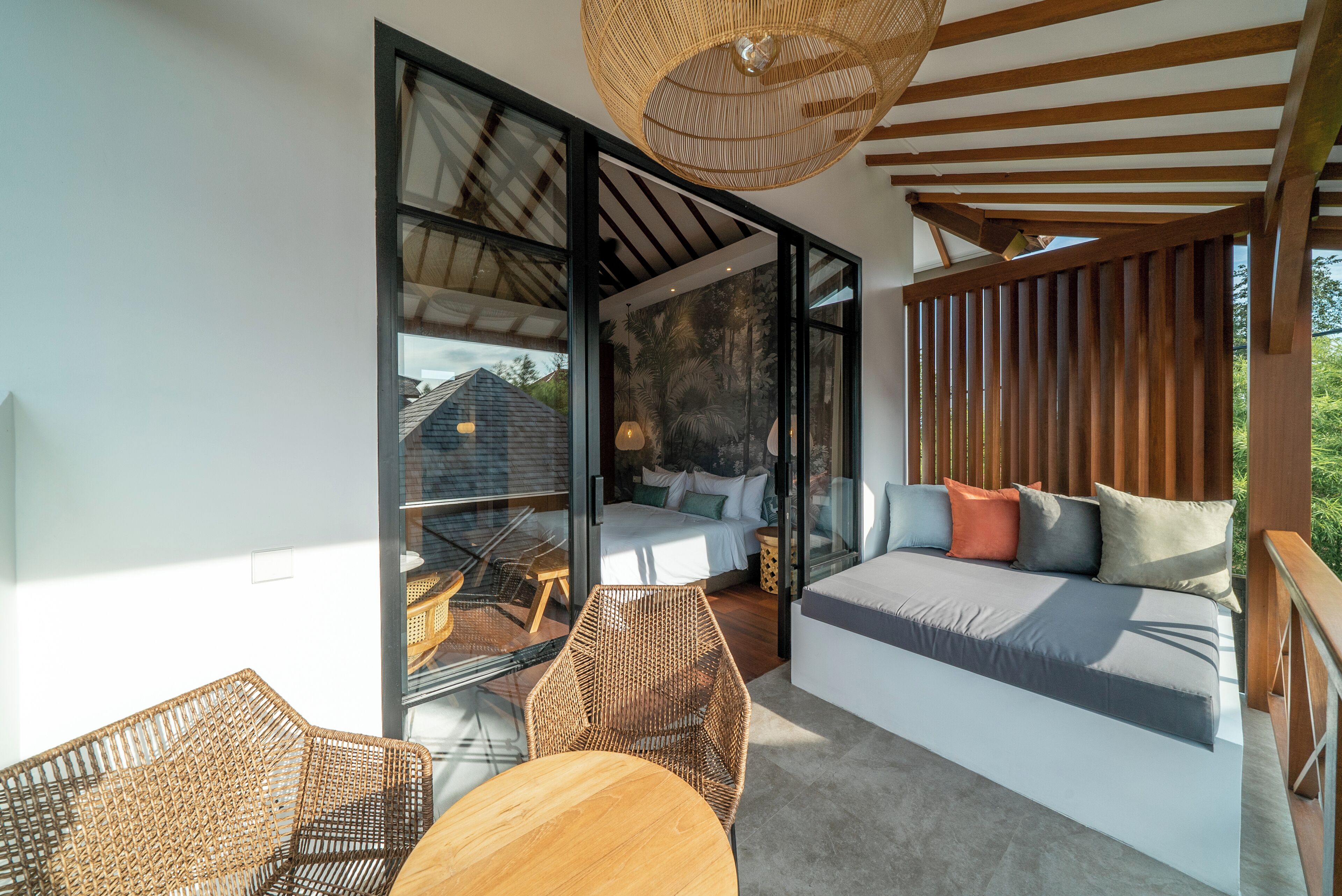 A modern room with a large sliding glass door leading to a balcony, a sofa with cushions, wicker chairs, and a hanging light fixture.