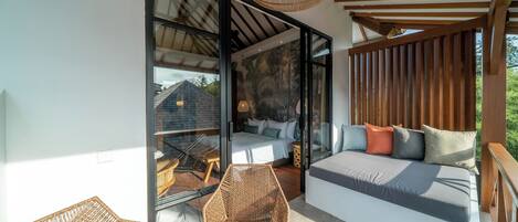 A modern room with a large sliding glass door leading to a balcony, a sofa with cushions, wicker chairs, and a hanging light fixture.