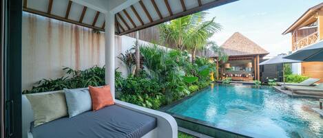 A modern outdoor pool area with a built-in seating area and lush greenery.