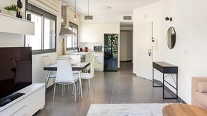 A modern kitchen with white cabinetry, a dining area with a table and chairs, and a view of the outdoors through a large window. - Luxury Oasis Tel Aviv Beach

2BD Apt & Parking 2 minute walk from the beach (Tel Aviv-Yafo)
