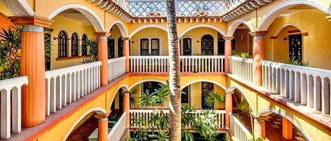A courtyard with a central palm tree, surrounded by balconies with railings and potted plants.