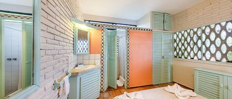 A bedroom with a brick wall, a bed with towels, a bathroom with a sink and mirror, and a window with a patterned view.
