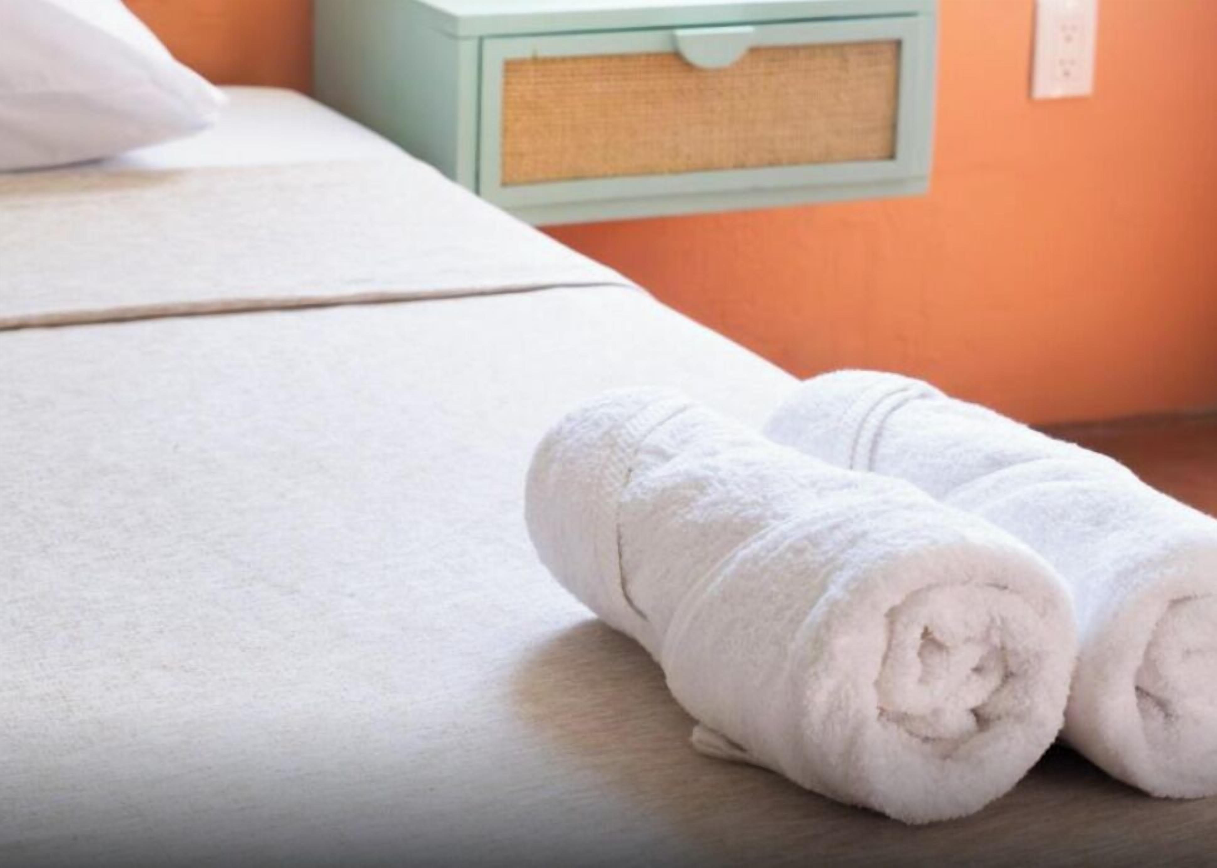 Uma cama bem arrumada com lençóis brancos e uma toalha enrolada ao lado.