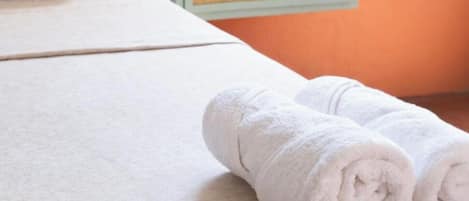 Uma cama bem arrumada com lençóis brancos e uma toalha enrolada ao lado.