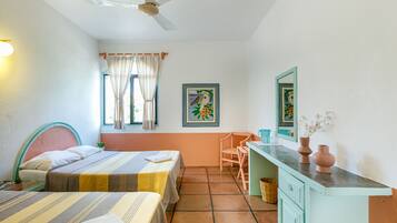 Una habitación con dos camas, un escritorio, una silla, un ventilador de techo y una ventana con cortinas.
