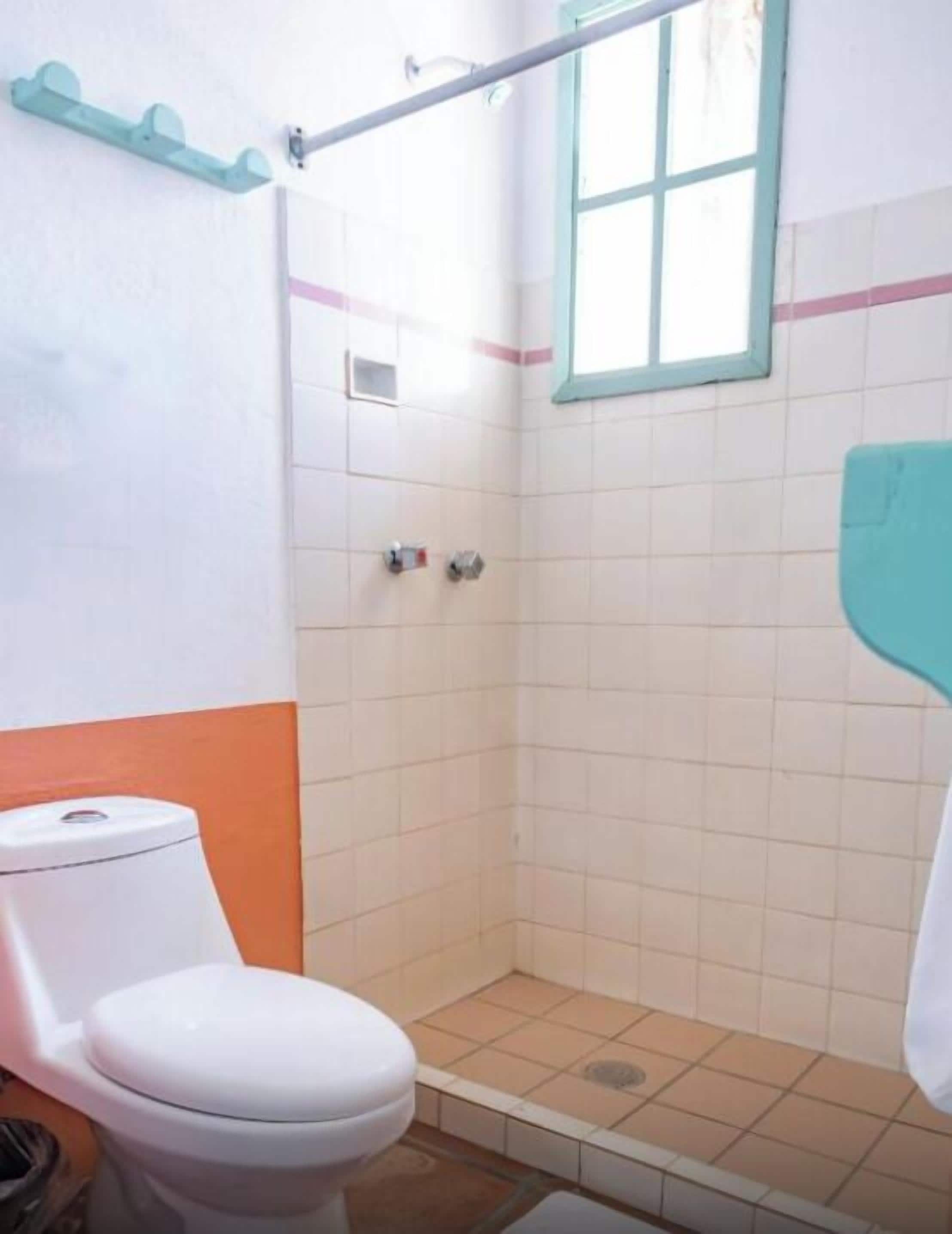 A small bathroom with a toilet, a shower stall, and a window.