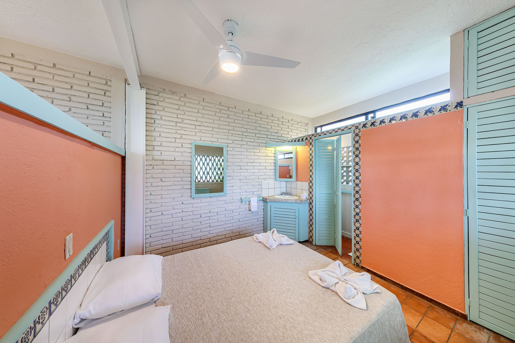 Habitación de hotel con cama, baño con lavabo y espejo, y ventilador de techo.