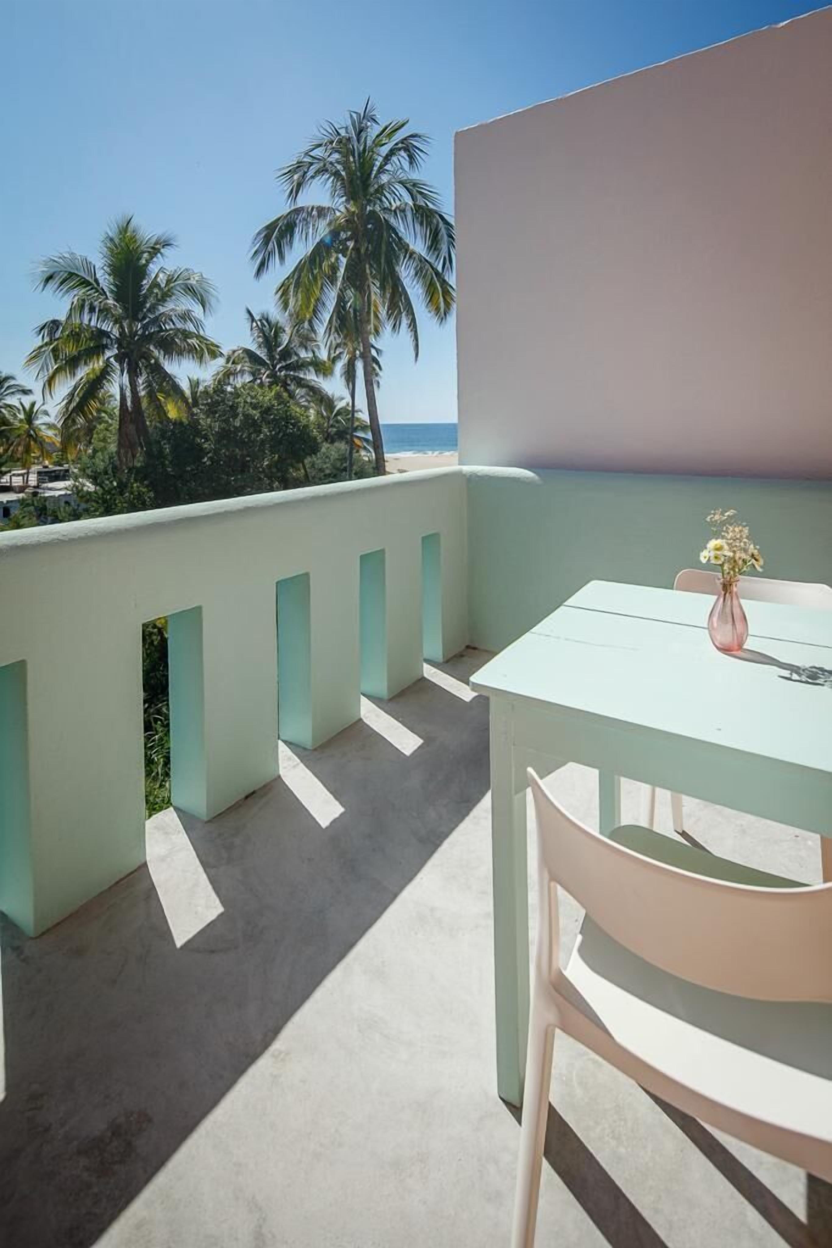 Un balcon avec une table et une chaise, d’où l’on peut admirer des palmiers et une plage.