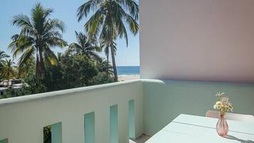 Un balcón con mesa y silla, con vistas a palmeras y una playa.