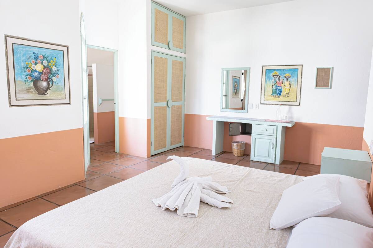 Una habitación de hotel con cama, escritorio y baño visible a través de una puerta abierta.