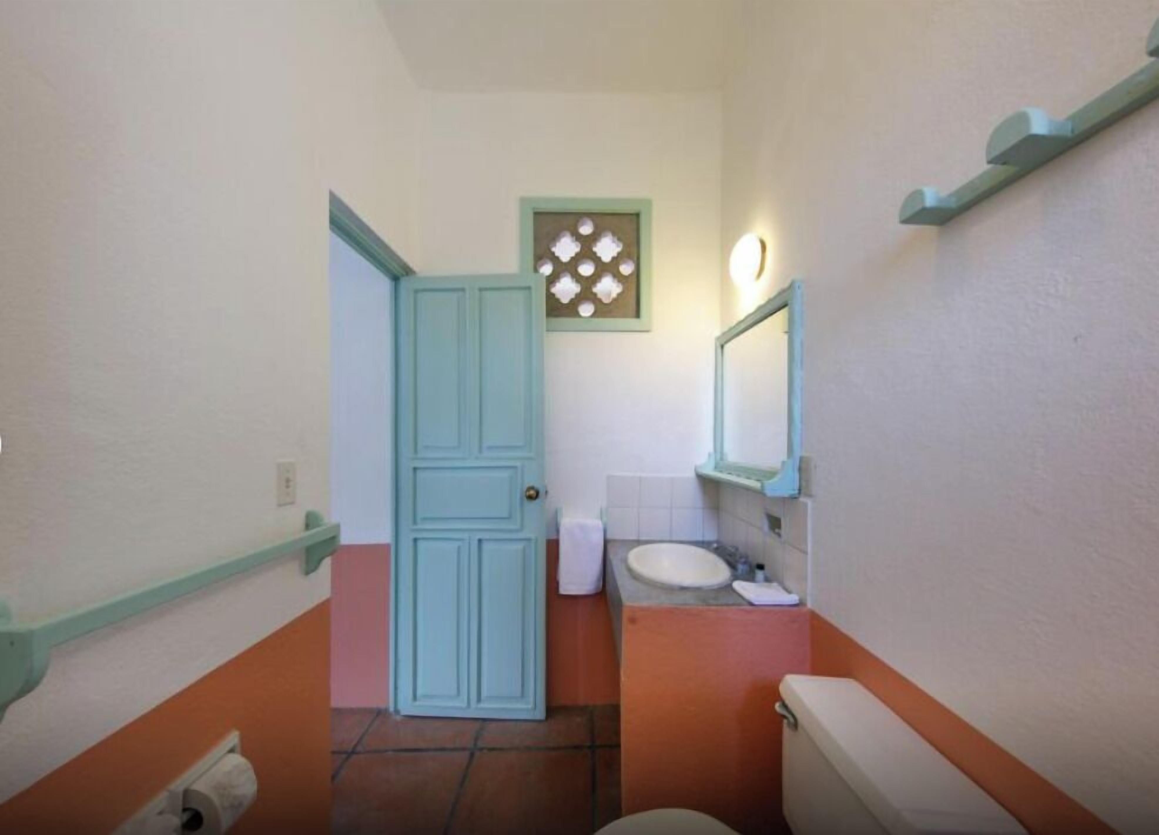 Une petite salle de bain comprenant des toilettes, un lavabo et une porte donnant sur une autre pièce.