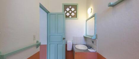 Une petite salle de bain comprenant des toilettes, un lavabo et une porte donnant sur une autre pièce.