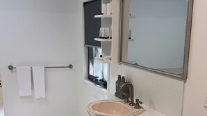 Bany amb un lavabo blanc, un mirall i una petxina amb productes de tocador.