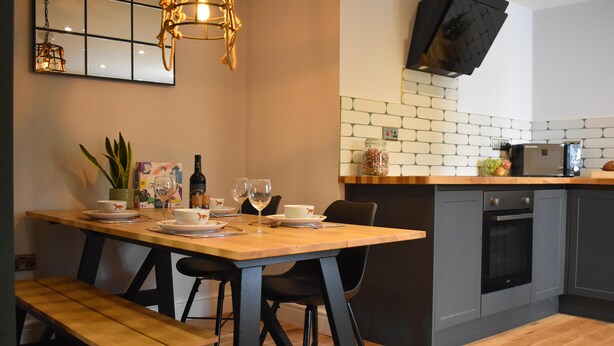 A modern kitchen with a wooden dining table, black chairs, and a built-in oven.