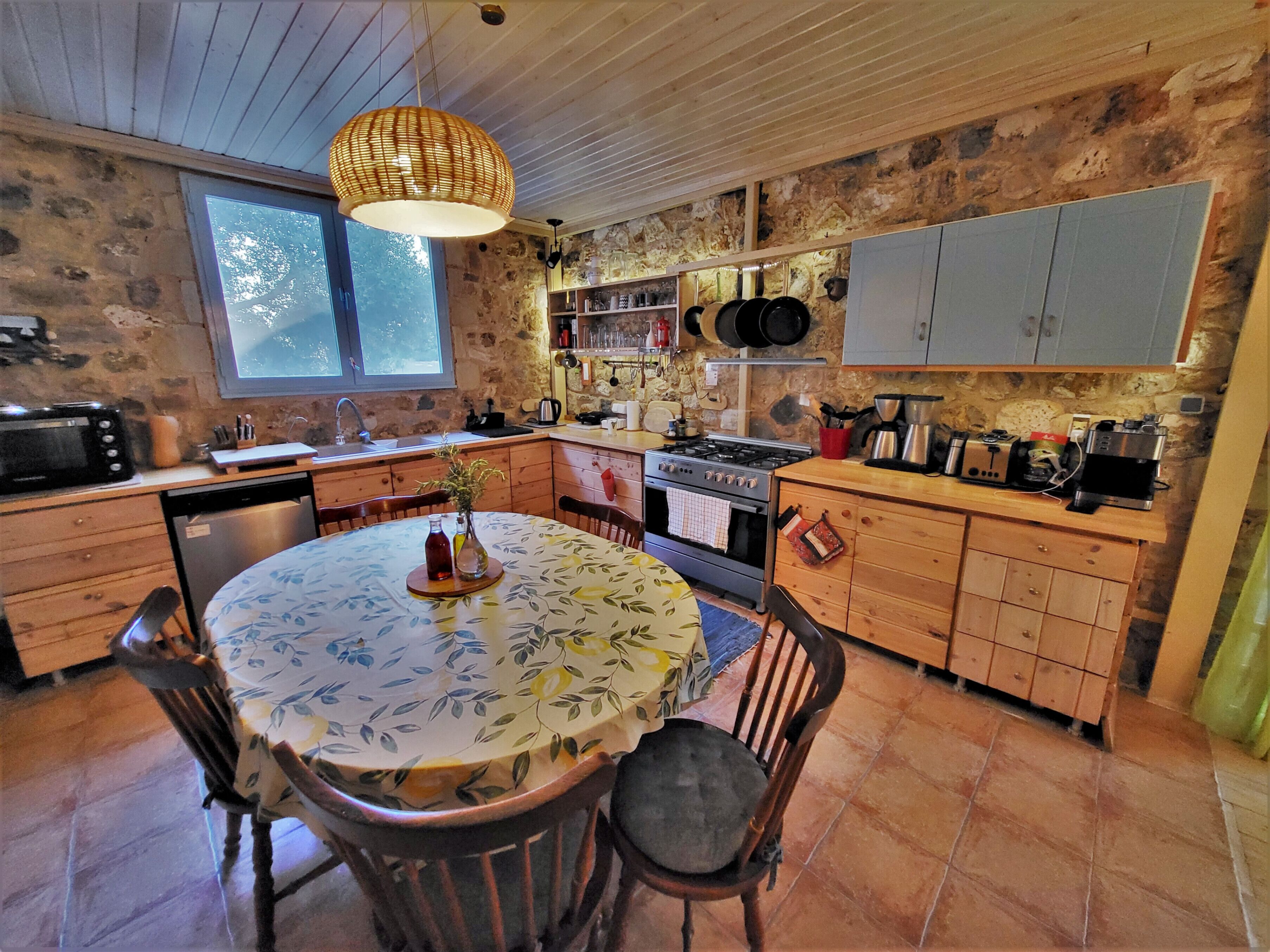 Una cocina rústica con una mesa redonda, armarios de madera, una estufa y varios utensilios de cocina.