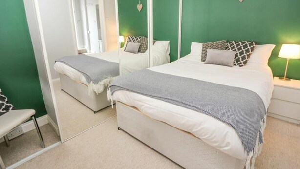 A bedroom with a large bed, a bedside table, a chair, and a mirror. - Stunning 1-Bed Apartment in Southsea (Southsea)