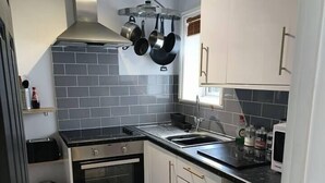 A compact kitchen with white cabinets, a black countertop, a stainless steel oven, and a black trash bin. - Stunning 1-Bed Apartment in Southsea (Southsea)
