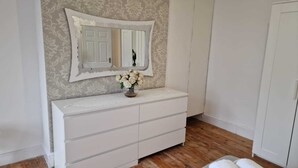 A white dresser with a mirror above it, a vase with white flowers, and a wooden floor.