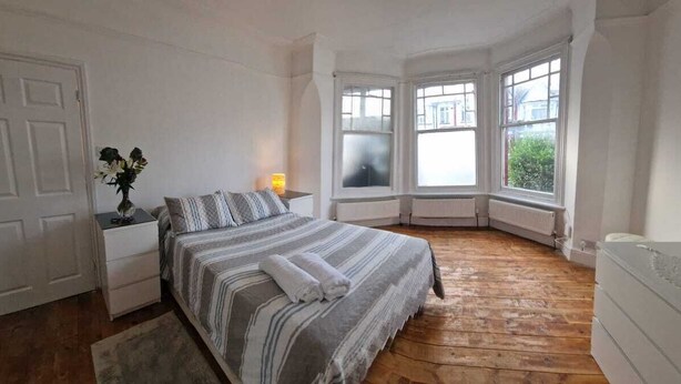 A bedroom with a large bed, a nightstand, a lamp, and a window with a view of the outside.