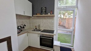 A compact kitchen with white cabinets, a black countertop, a built-in oven, and a window overlooking a backyard.