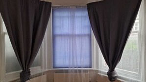 A room with a large window, dark curtains, and a radiator below.