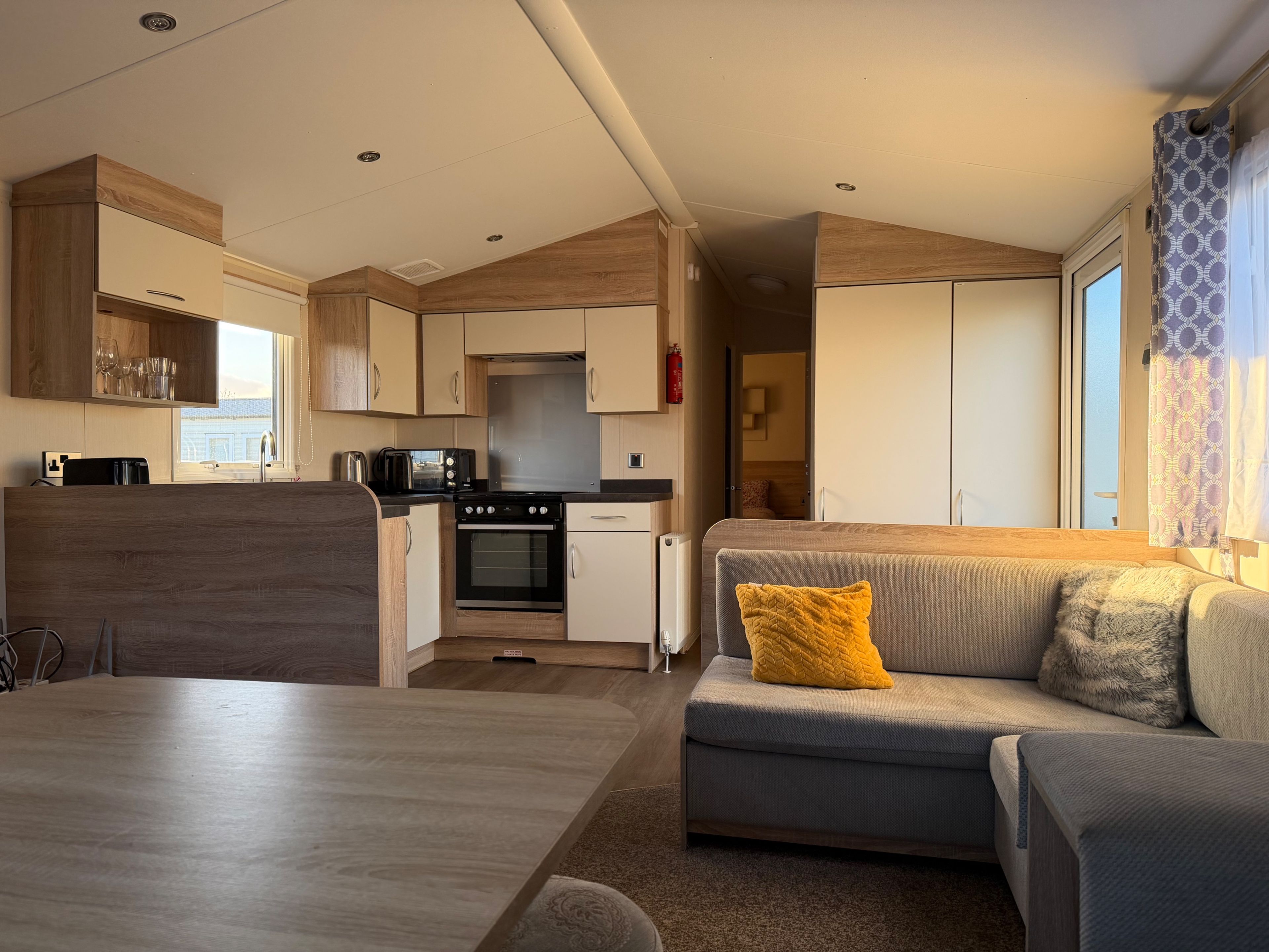 Un espace de vie compact comprenant un coin cuisine, un canapé avec un coussin jaune et une table à manger.