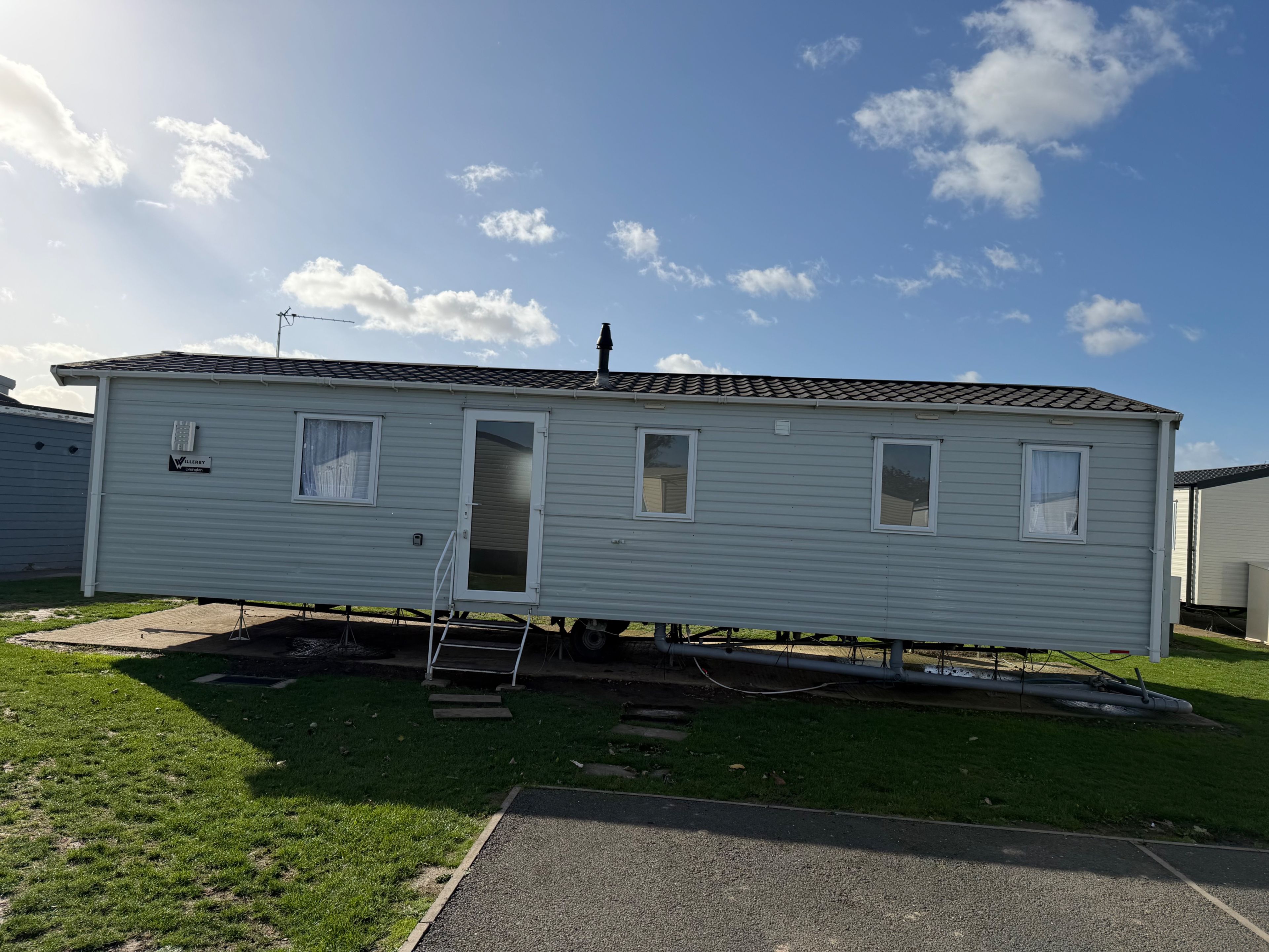 Une maison mobile avec une seule porte et deux fenêtres, située sur une pelouse, sous un ciel dégagé.