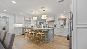 Een moderne keuken met witte kasten, een centraal eiland met barkrukken, hanglampen en roestvrijstalen apparatuur.