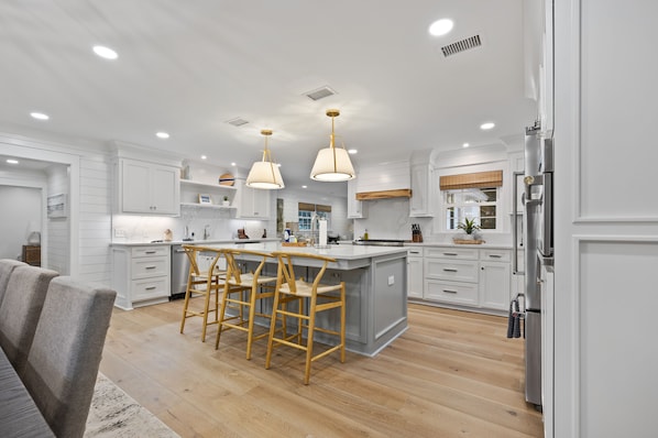 A modern kitchen with white cabinetry, a central island with bar stools, pendant lighting, and stainless steel appliances.