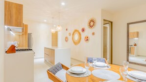 A modern dining area with a wooden table set for four, a kitchen in the background, and decorative wall art. - Santamar by TAO (Akumal)