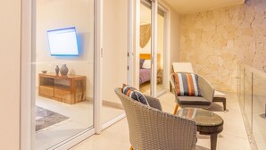 A balcony with wicker chairs, a glass table, and a view of a bedroom with a bed and a TV. - Santamar by TAO (Akumal)
