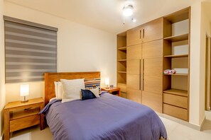 A bedroom with a bed, nightstands, a wooden wardrobe, and a window with blinds. - Santamar by TAO (Akumal)