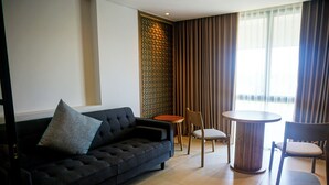 A modern living room with a dark sofa, a round table, and two chairs. - Nusa Dua Suites Bali powered by Cocotel (Nusa Dua)