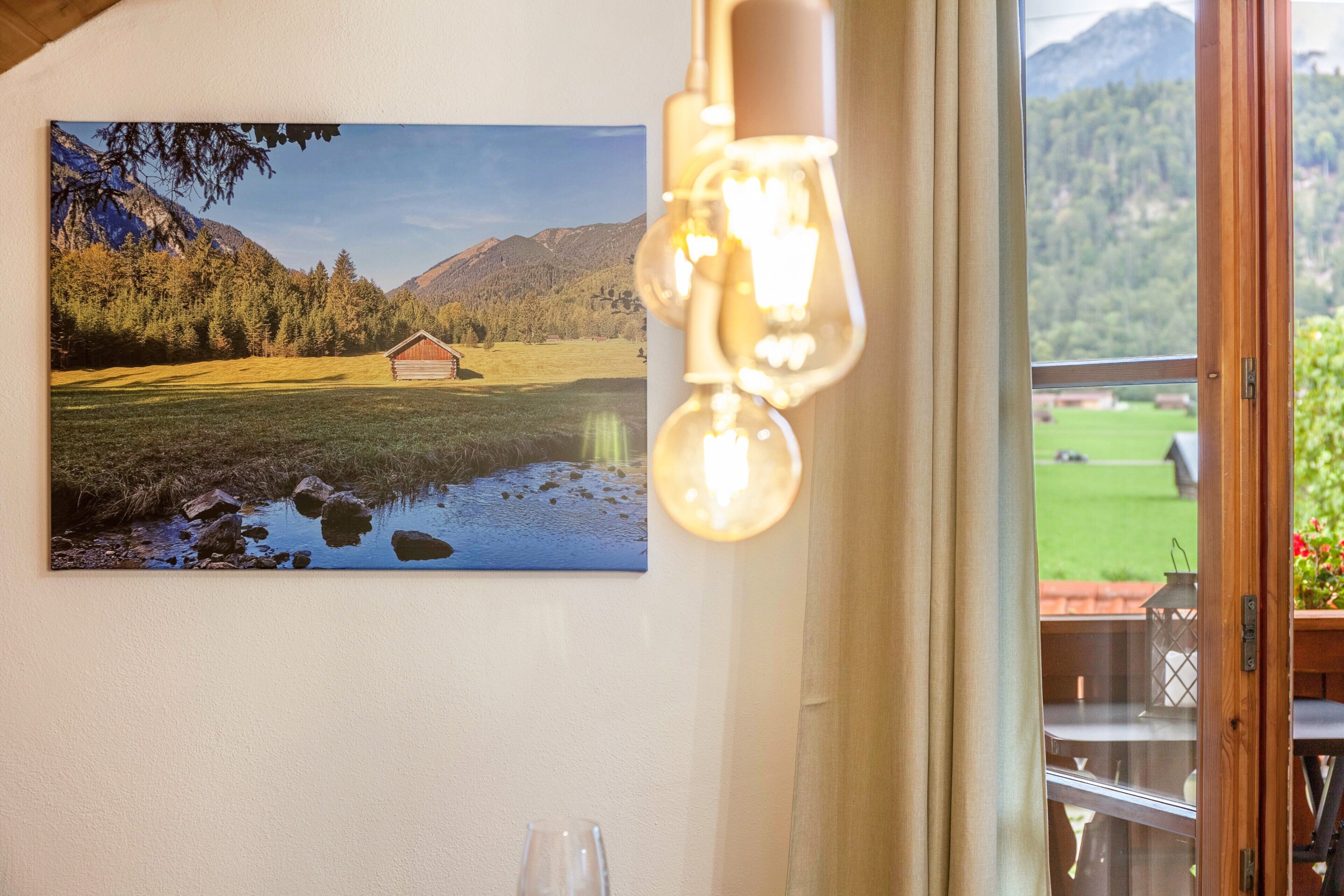 Una stanza con un quadro che raffigura un paesaggio montano, un lampadario e vista attraverso una finestra.