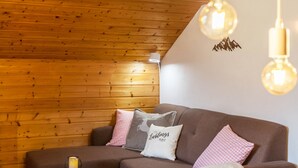 Un techo de madera, un sofá marrón con almohadones a cuadros y dos lámparas colgantes.