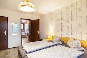 Une chambre d’hôtel avec deux lits, une porte en bois, une salle de bain visible à travers une porte ouverte et un mur orné d’un motif.