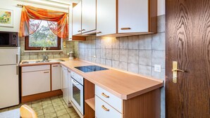 Une cuisine dotée d’un plan de travail en bois, de meubles blancs, d’un four encastré et d’une fenêtre avec un rideau.