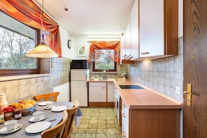 A compact kitchen with a dining area, a refrigerator, a sink, and a window with curtains.