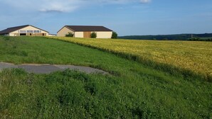 Paisatge rural amb dues construccions, una amb garatge i l'altra amb terrat pla, envoltat de camps i un cel serè.