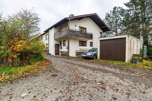 Une maison à deux étages avec un balcon, une allée en gravier et une voiture garée.