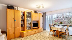 Habitació amb un armari de fusta, televisió, taula de dinar amb cadires i finestra amb cortines.