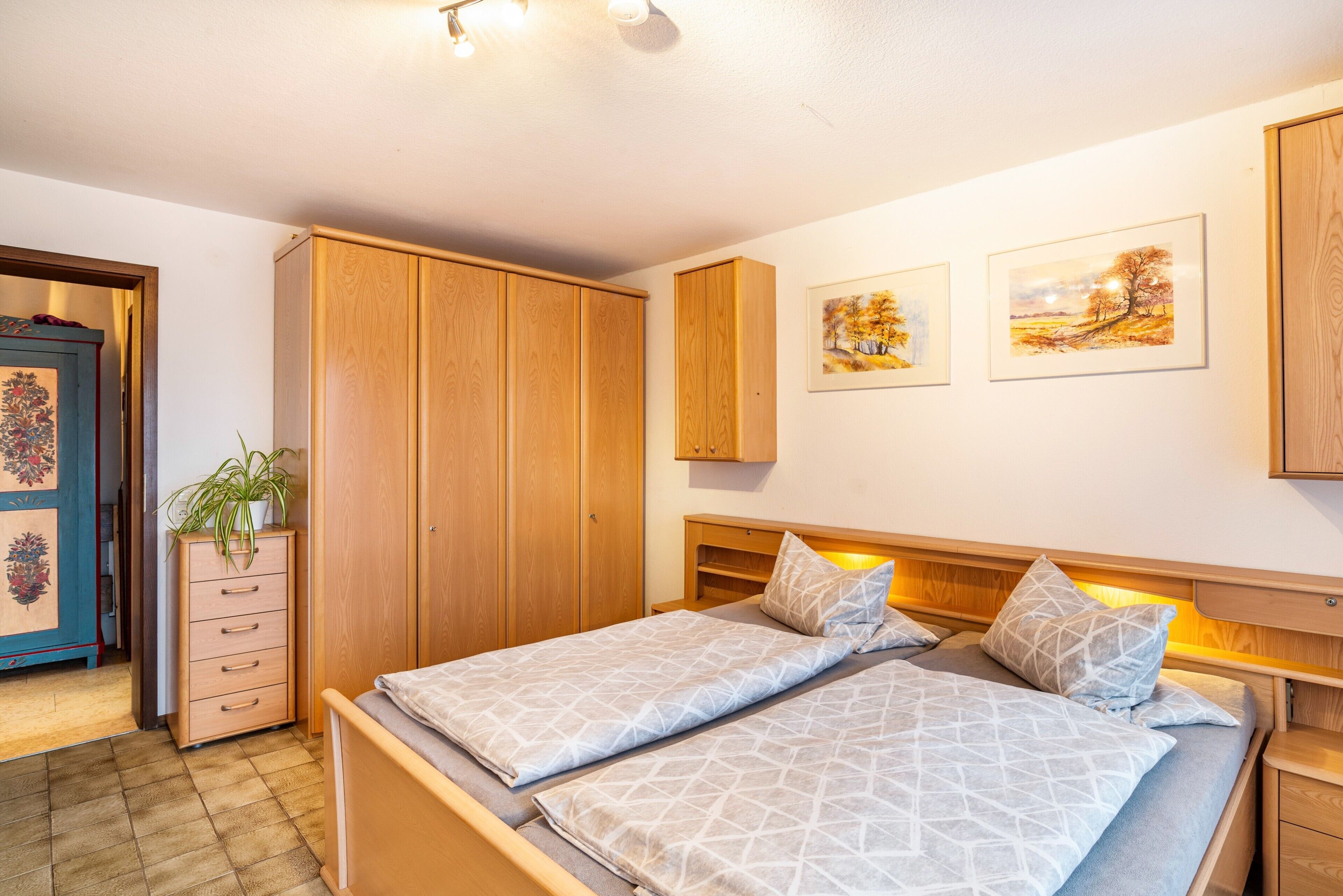 A bedroom with two beds, wooden wardrobe, and artwork on the wall.