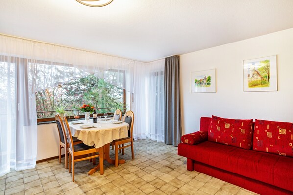 Un coin repas avec une table et des chaises, un canapé rouge et deux tableaux encadrés au mur.