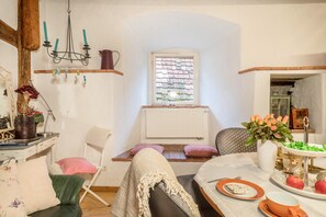 Une pièce chaleureuse avec une table à manger dressée, une fenêtre donnant sur un beau paysage, un radiateur et un lustre.