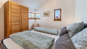 Een slaapkamer met een grote inbouwkast, twee bedden, een raam en een schilderij aan de muur.