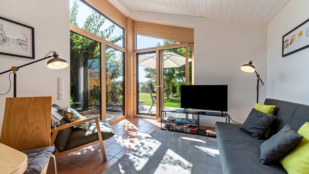 Een moderne woonkamer met een bank, een fauteuil, een televisie en een groot raam.
