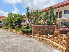 A hotel entrance with a sign, a paved walkway, and a landscaped garden with palm trees and shrubs. - Thai Ngam Palace Hotel (Kaeng Khlo)