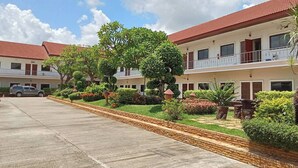 A hotel with a red-tiled roof, multiple balconies, and a well-maintained garden with various plants and shrubs. - Thai Ngam Palace Hotel (Kaeng Khlo)